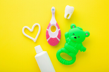 Green rubber teddy bear, white heart shape, tooth, tube of toothpaste, pink toothbrush on bright yellow table background. Things for babies teeth cleaning through fun. Closeup. Top down view.