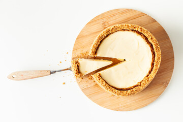 Homemade classic New York cheesecake cut on the wooden board. Vanilla pie with cheese and crunchy crust on the whiite background. Close up, macro shot