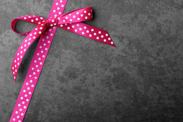 Pink spotted bow and ribbon on texture dark background with copy space