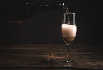 A hand with a bottle pours champagne into a glass on a dark wooden background. Concept of alcoholic beverages.