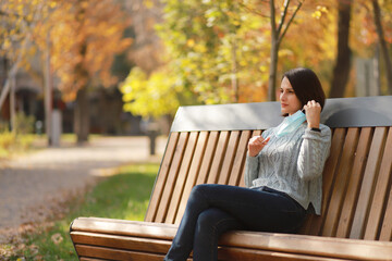 Fototapeta premium Beautiful woman in medical protective face mask sitting on a bench in autumn park. Coronavirus social distance concept.