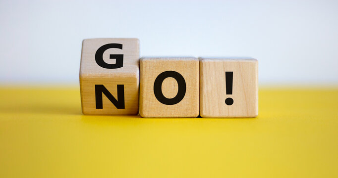 Hand turns wood blocks and changes the word 'no' to 'go'. Beautiful yellow table, white background, copy space. Business concept.