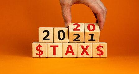 Business concept of planning 2021. Male hand flips wooden cubes and changes the inscription 'Tax 2020' to 'Tax 2021'. Beautiful orange background, copy space.