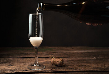The champagne glass is just beginning to fill with alcohol with foam and bubbles on a wooden...