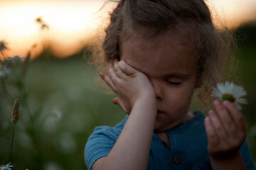 Portrait of a curly girl on a bright sunset background. The girl rubs her eye with the hand.