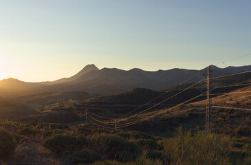 Puesta de sol en un paisaje de montaña. Un tendido eléctrico refleja la luz mientras se aleja hacia el pico Espigüete.