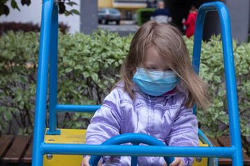 Fototapeta na wymiar Portrait of a cute blonde little girl wearing a Medical Disposable Face Mask, playing on a playground during quarantine. Stay at home. Isolation. Coronavirus and Air pollution concept.