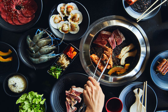 Faceless lady roasting meat with tongs on grill in restaurant