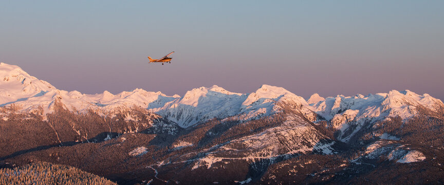 A single engine airplane flying through snowy mountains at sunset