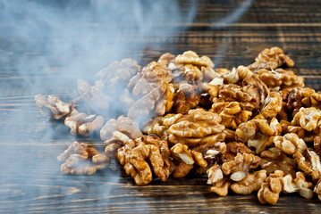 Walnut texture with steam close up. Many halves of peeled nuts on an old wooden board. Food in blue smoke on a background of shabby brown board.