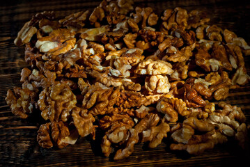 Walnut texture close up. Many halves of peeled nuts on an old wooden board. Food on a background of shabby brown board. Contrasting dramatic light as an artistic effect.