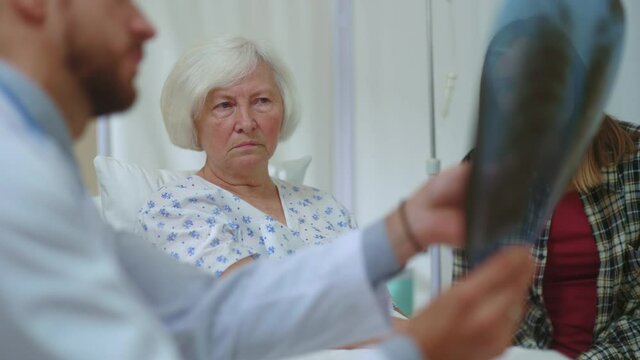 Doctor telling bad news disappointing diagnosis to female patient. Shocked old woman discovering lung cancer looking on x-ray image refusing expensive therapy.
