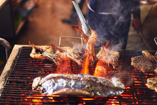 Faceless cooker frying crayfishes on grill in outdoors market