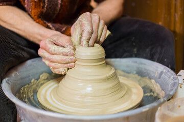 Close up view - professional male potter working with clay on pottery wheel in workshop, studio....