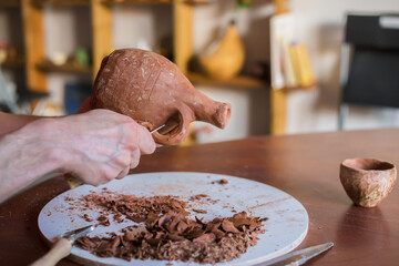 Professional male potter shaping and scraping dry clay jug with special tool in pottery workshop, studio. Crafting, artwork and handmade concept