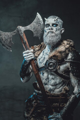 Frozen dead warrior with horns and white skin in dark armour holding two handed axe in twilight.