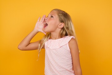 Beautiful Caucasian young girl standing against yellow background profile view, looking happy and...