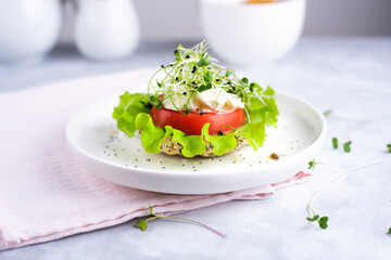 Veggie burger with tomato, lettuce and microgreens on a white plate with  cereal bun on a white background