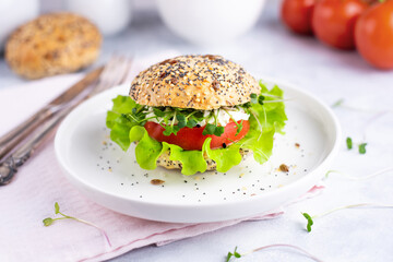 Veggie burger with tomato, lettuce and microgreens on a white plate with tomatoes, cereal bun on a white background