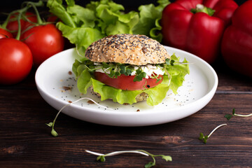 Vegetarian burger with green, red vegetables and microgreens on a white plate on a dark wooden background, close up