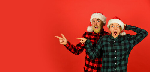 Fototapeta premium Idea for fun. Good mood. Winter joy. Couple in love pointing copy space. Look at this. Santa Claus style. Christmas time. Man and woman christmas holiday celebration. Family shopping. Christmas party