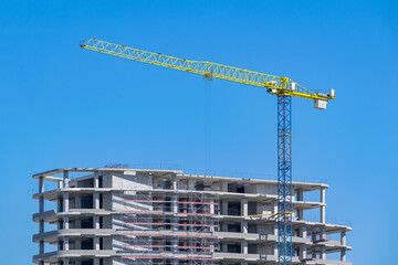 Tower crane in front of a building under construction against the backdrop of a clear sky.