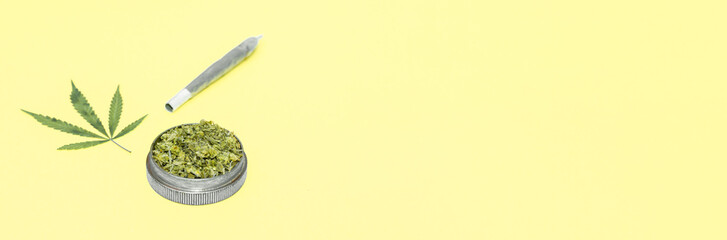 Big marijuana joint, grinder full of chopped cannabis and leaf on yellow background.
