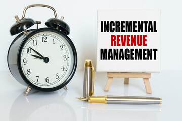 On the table there is a clock, a pen and a stand with a card on which the text is written - INCREMENTAL REVENUE MANAGEMENT