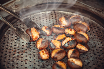 Costermonger roasting sweet chestnuts with tongs on counter. Famous traditional Turkish fried chestnuts on the counter of street seller.
