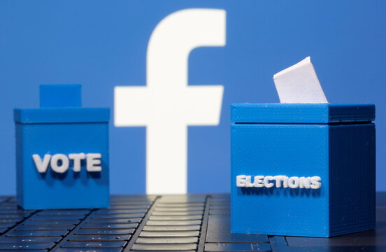 3D printed ballot boxes are seen in front of a displayed Facebook logo