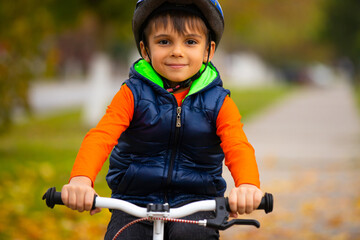 Obraz premium Preschool child posing in a helmet and on a bicycle pedal in the autumn park. Active healthy outdoor sports