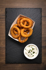 takeaway container with fried onion rings. fried onion rings on slate cutting board with mayonnaise and parsley.