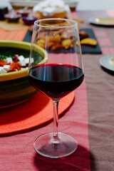 glass of red wine on an orange-colored table cloth, behind it is a salad and barbecued meat. foodie
