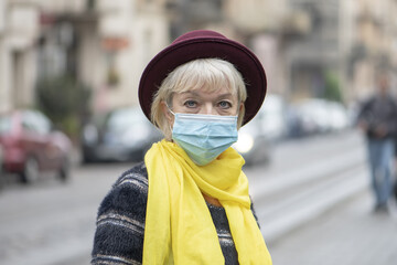 Elderly retired woman 60-65 years old in a medical mask on the background of the city landscape. Concept: risk of disease, risk group,