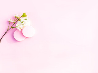 Cosmetic sponges and tree branch with spring flowers on pink background.