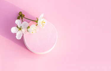 Cosmetic sponges and tree branch with spring flowers on pink background.