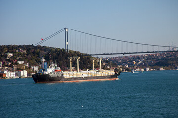 Ship sailing under the Bosphorus Bridge with background of Bosphorus strait on a sunny day with background blue sky and mosque in Istanbul, Turkey. Blue Turkey concept.