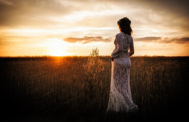 A pregnant woman in a delicate negligee in a field enjoys a beautiful sunset. Beauty and tender motherhood.