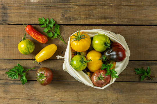 Different raw ripe fresh tomatoes in linen bag. Concept of green house life style and products of subsistence farming, flat lay on dark wooden rustic surface, copy space