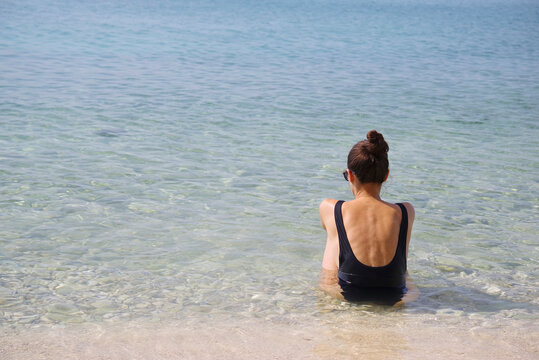 Beautiful young tanned girl  sits on the shore of a paradise white sand beach with bruise color in the sea
