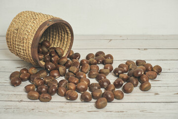 Fresh chestnuts in the basket falling on a white wooden table