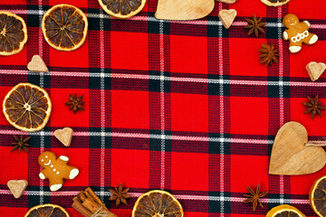 Fototapeta na wymiar Christmas greeting card. Gingerbread men, sugar hearts, cinnamon sticks and star anise on a red tartan background. Text space.