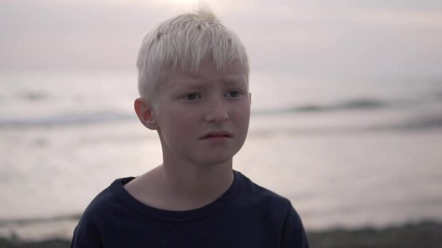 Close-up of the face of a beautiful brooding baby boy blond against the sea at sunset.
