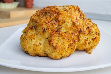 Composition in natural light. Large cauliflower baked with cheese and spices. On a white glossy...