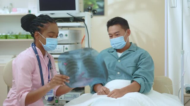 Quarrel at hospital. African american woman doctor consulting male patient. Confused angry asian man quarrelling while examining lungs x-ray. Medical. healthcare concept.
