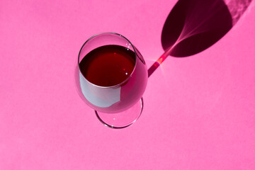 a glass of pink red wine on pink background with sparkling shadows. Free copy space.  Concept of organic drinks.