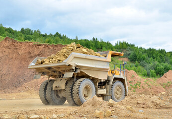 Obraz premium Mining truck and excavators working in the limestone open-pit. Loading and transportation of minerals in the dolomite mining quarry