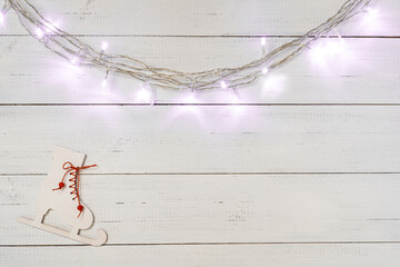 Christmas garland lights and wooden skates toy on white wooden boards background.