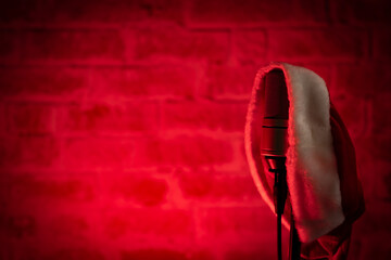 A Christmas concert photo with Santa Claus's hat hanging on a microphone, red spotlights and a brick wall in the background with copy space