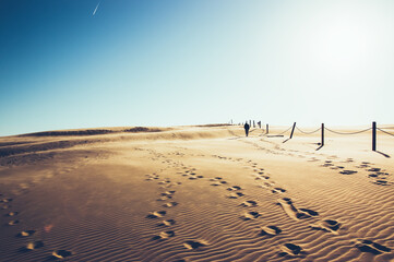 Krajobraz pustynny błękitne niebo i ruchome piaski  z sylwetką idącego człowieka w pięknym świetle zachodzącego słońca - obrazy, fototapety, plakaty